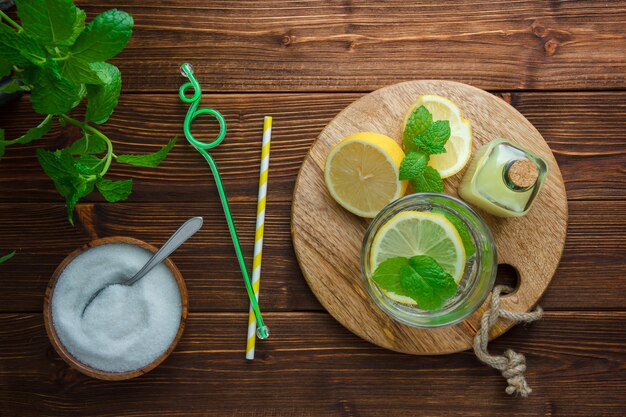 Set of leaves, wooden knife, cutting board, bowl of salt and half of lemon on a wooden surface. top view.