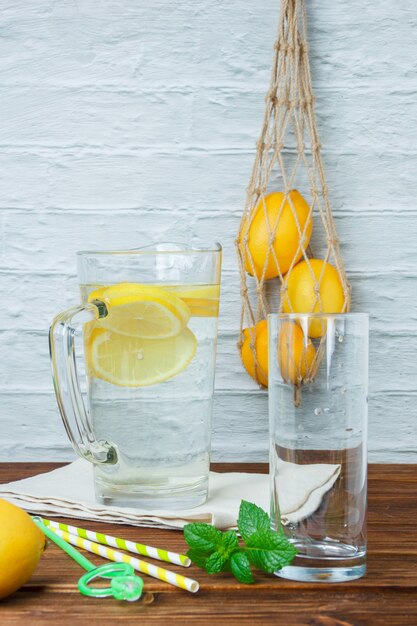 Set of lemons, leaves and carafe of lemon on a white cloth on a wooden and white surface. side view.