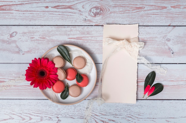 Set of macaroons and flower on plate near paper and petals