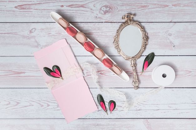 Set of macaroons near paper, petals and mirror