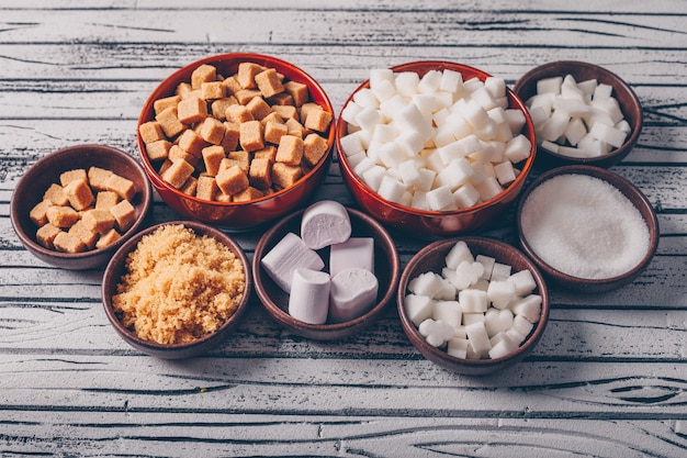 Set of marshmallow and white and brown sugar in bowls on a light wooden table. high angle view.