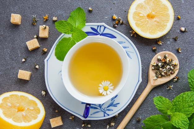 Set of mint leaves, sugar, lemon and chamomile herbs in spoon and a cup of chamomile tea