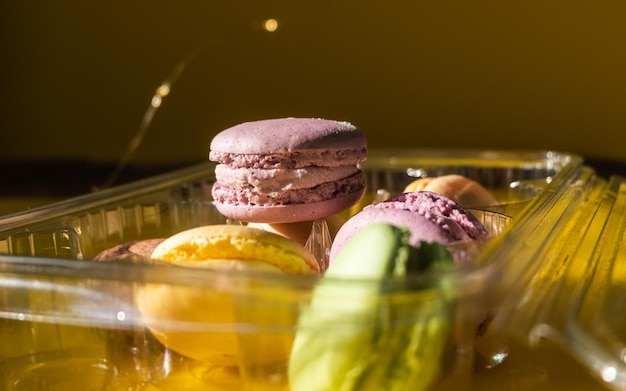 Set of multiple colorful macarons in a plastic container yellow background and sparkles in the dark