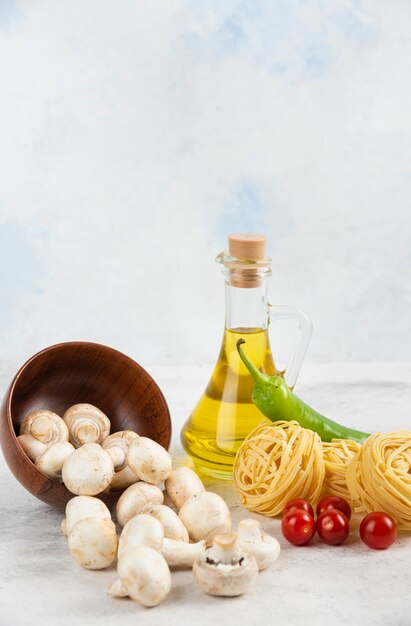 Set of mushrooms, extra virgin olive oil, pastas, cherry tomatoes and chili peppers on a piece of marble.