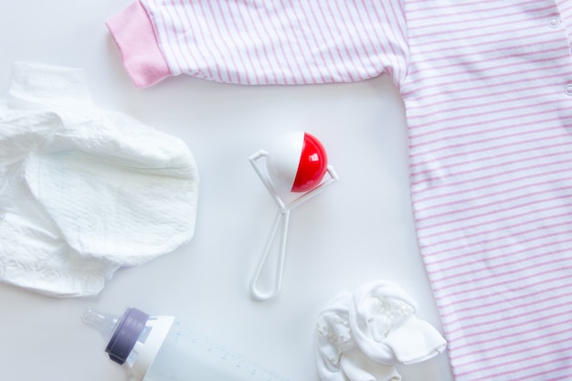 Set of newborn supplies on table: diaper, beanbag, bottle, suit