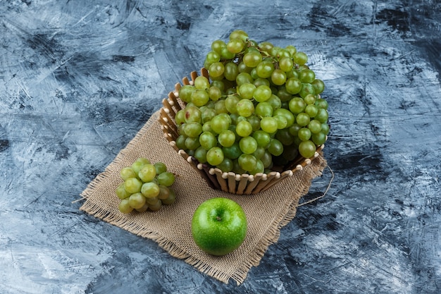 Бесплатное фото Набор яблока и зеленого винограда в корзине на фоне гранж и кусок мешка. высокий угол обзора.