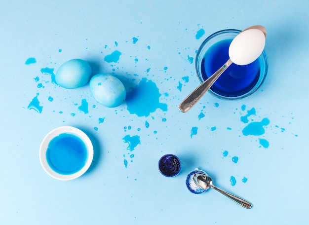 Набор синих пасхальных яиц между кляксами, ложкой и красящей жидкостью