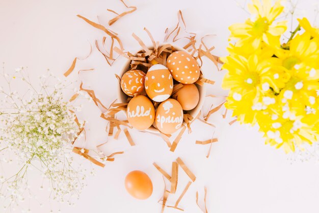 Set of orange Easter eggs in bowl between fresh flowers