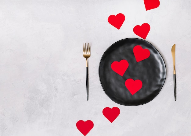 Набор украшений сердца на черной тарелке между столовыми приборами