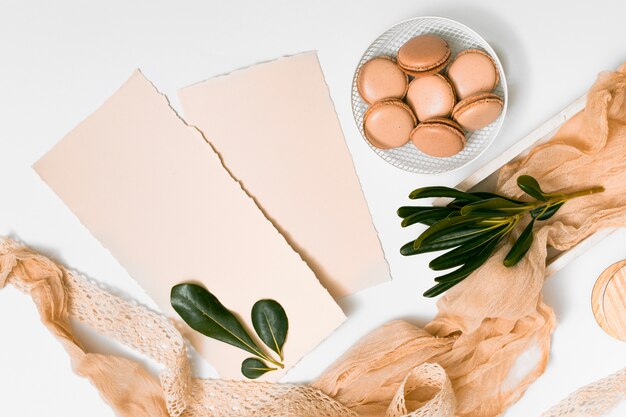 Set of papers and macaroons on plate near textile and plant twigs