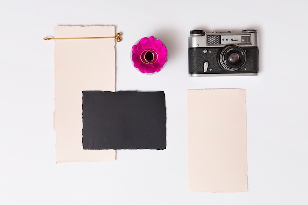 Set of papers near fresh flower with rings on plate and retro camera