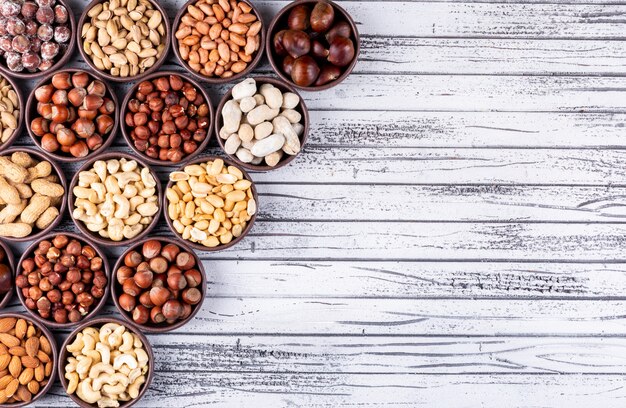 Set of pecan, pistachios, almond, peanut, and assorted nuts and dried fruits in a cycle shaped mini different bowls on a white wooden table