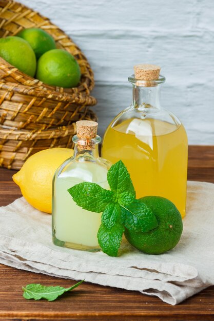 Set of on piece of white cloth, lemon leaves and lemon and juice in a basket on a wooden surface. high angle view.