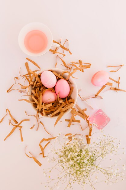 Set of pink Easter eggs in bowl between flowers and cans of dye liquid