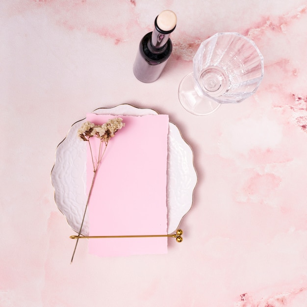 Set of plant twig and paper on plate near bottle and glass