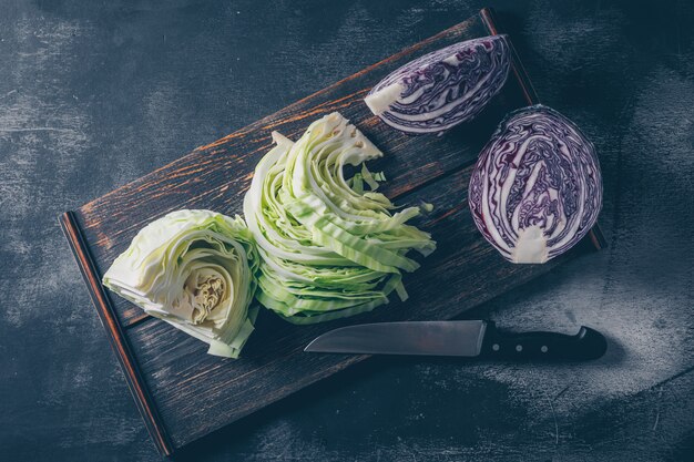 Set of red cabbage and knife and sliced and chopped cabbage in a cutting board on a dark textured background. top view.