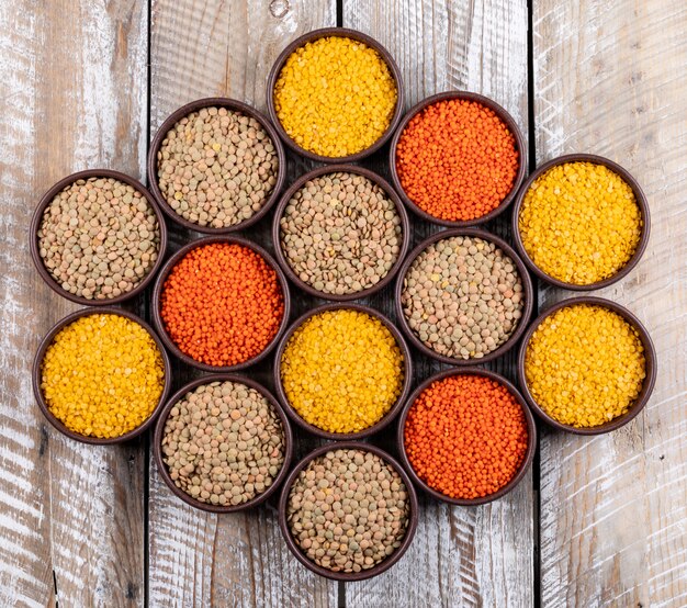 Set of redf, yellow, green lentils and different lentils in a brown bowls on a beige wooden table. top view.