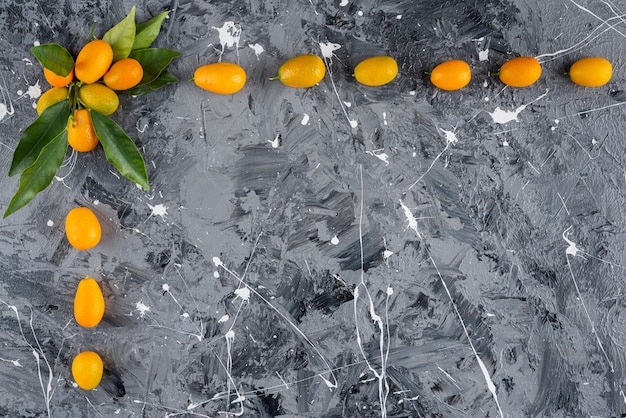 Set of ripe kumquats with green leaves on marble background.