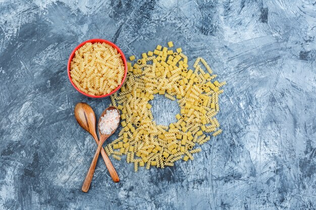 Set di sale in cucchiaio di legno e pasta assortita in una ciotola su uno sfondo di gesso grungy. laici piatta.