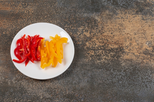 Free photo set of sliced red and yellow peppers on white plate.