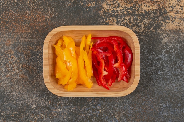 Set of sliced red and yellow peppers on wooden plate.