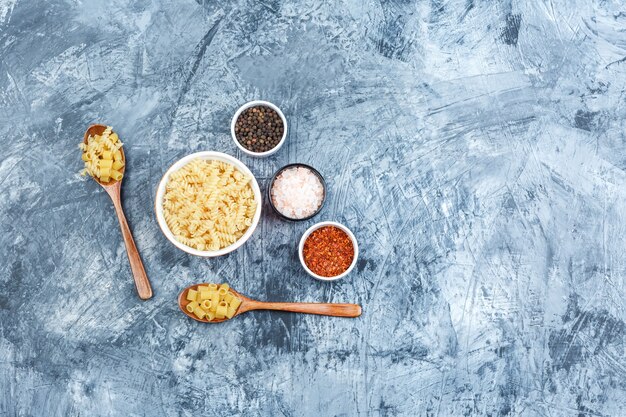 Set of spices and assorted pasta in bowl and wooden spoons on a grungy plaster background. flat lay.