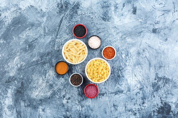 Set of spices and assorted pasta in bowls on a grey plaster background. top view.