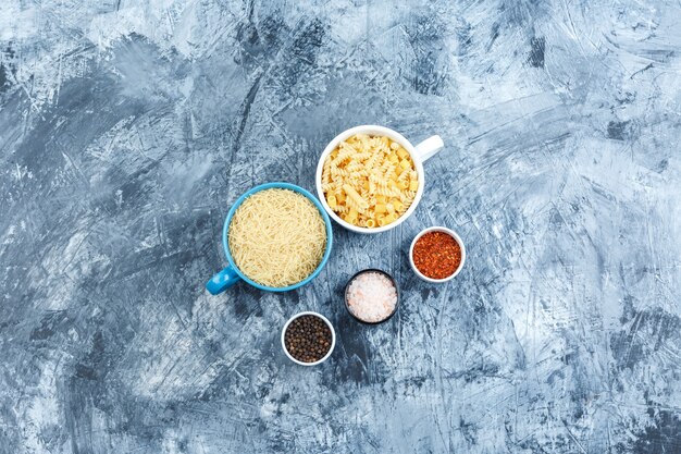 Set of spices and assorted pasta in bowls on a grey plaster background. top view.