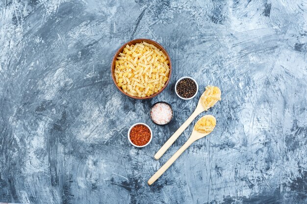 Set of spices and assorted pasta in clay bowl and wooden spoons on a grungy plaster background. flat lay.