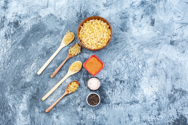 Free photo set of spices and assorted pasta in wooden spoons and bowl on a grungy plaster background. top view.