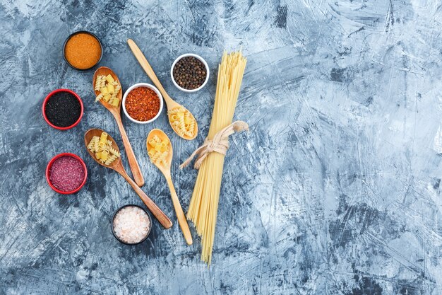 Set of spices and raw pasta in wooden spoons on a grey plaster background. top view.