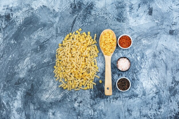 Set of spices and scattered pasta in a wooden spoon on a grungy plaster background. flat lay.