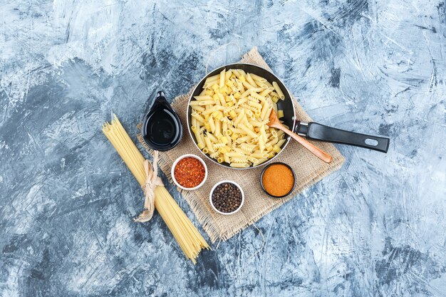 Set of spices, scoop, wooden spoon and raw pasta in a pan on plaster