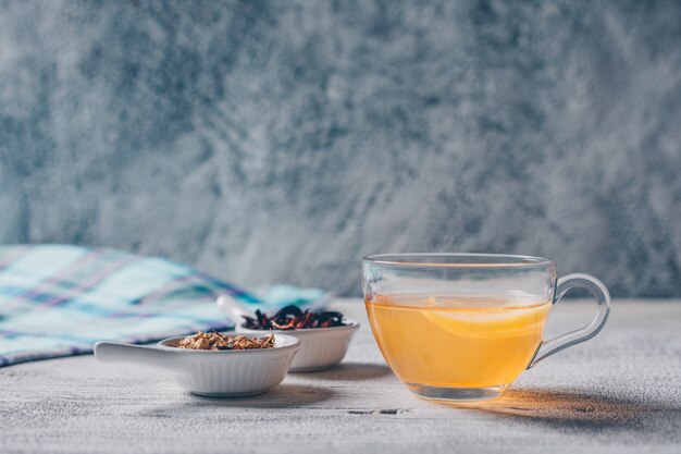 Set of tea herbs and orange colored water on a gray background. side view.