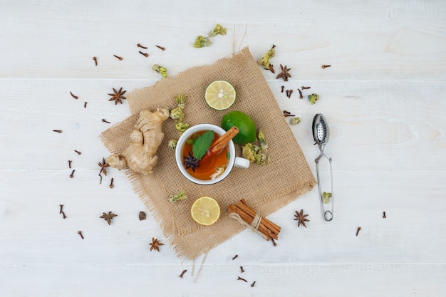 Set di un colino da tè e una tazza di tè, lime, zenzero e cannella in una tovaglietta di lino su una superficie grigia