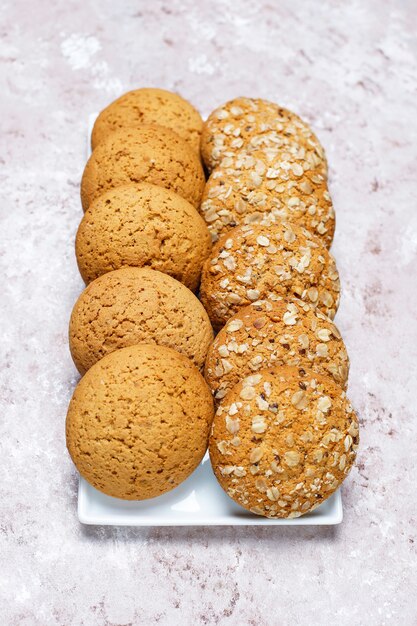 Комплект различных печений американского стиля на светлой конкретной предпосылке. Песочное печенье с конфетти, кунжутом, арахисовым маслом, овсянкой и шоколадным печеньем.