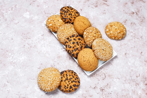 Set of various american style cookies on a light concrete background. Shortbread with confetti, sesame seed, peanut butter, oatmeal and chocolate chip cookies.