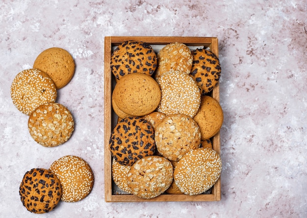 Foto gratuita insieme di vari biscotti di stile americano in vassoio di legno su fondo in cemento leggero. frollini con semi di sesamo, burro di arachidi, fiocchi d'avena e biscotti con gocce di cioccolato.