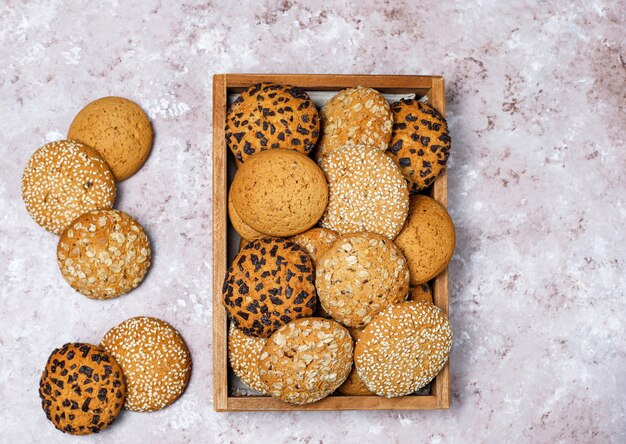 Set of various american style cookies in wooden tray on light concrete background. Shortbread with sesame seed, peanut butter, oatmeal and chocolate chip cookies.