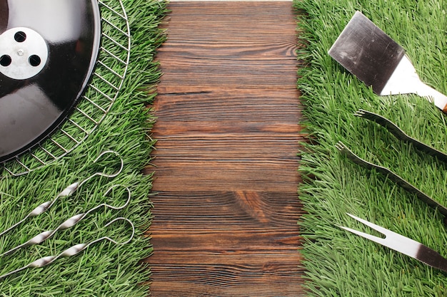 Set of various barbecue utensil on grass mat over wooden backdrop