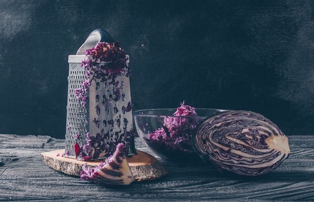 Set of vegetable grater and grated cabbage and red cabbage on a dark wooden background. side view.