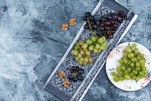 Set of walnuts and grapes in a plate on grunge and kitchen towel background. top view.