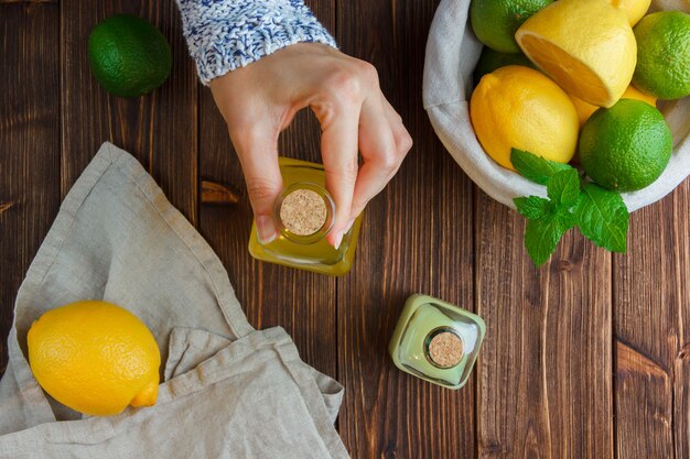 Set of white cloth, hands holding lemon juice bottle and lemons in a basket on a wooden surface. top view.