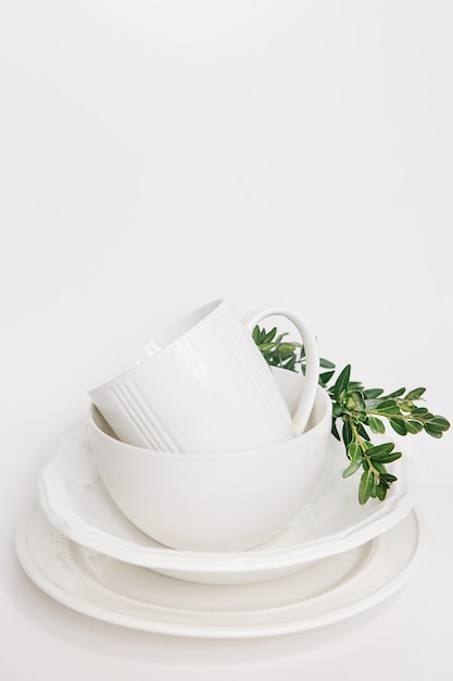 набор белых блюд из трех тарелок и чашка, украшенная ветвью эвкалипта