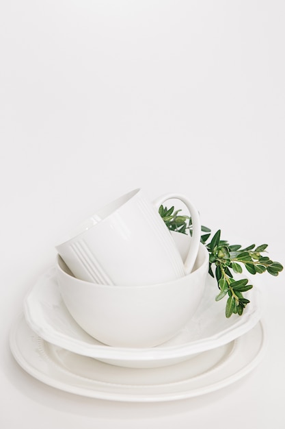 set of white dishes of three plates and a cup decorated with a branch of eucalyptus