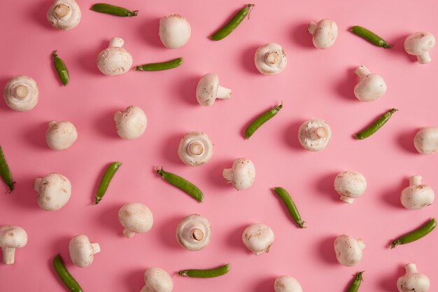 Set of white harvested champignons and green peas on pink background. Fresh vegetables for preparing delicious soup or pizza. Food photography. Raw ripe crops. Tasty mushrooms. Selective focus