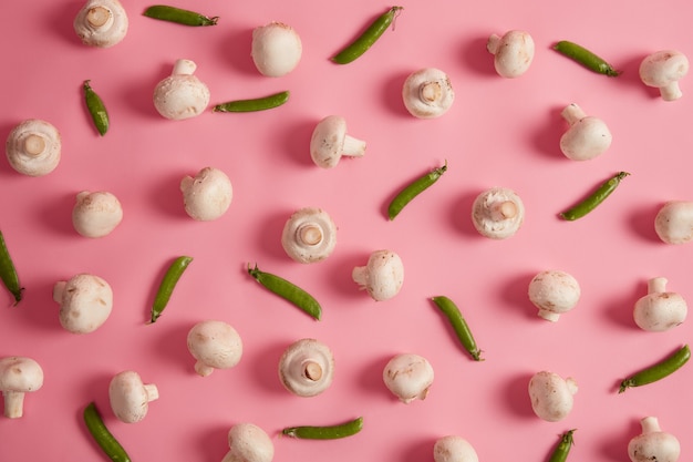 Набор белых собранных шампиньонов и зеленого горошка на розовом фоне. Свежие овощи для приготовления вкусного супа или пиццы. Фотография еды. Сырые спелые культуры. Вкусные грибы. Селективный фокус