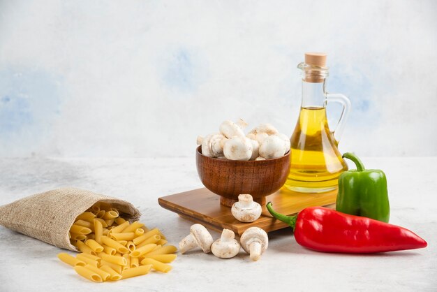 Set of white mushrooms, pastas, chili peppers and extra virgin olive oil on the marble.