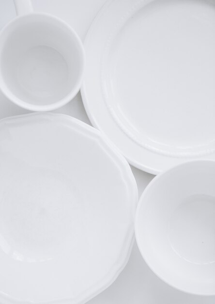 набор белой посуды из трех разных тарелок и чашка на белом фоне