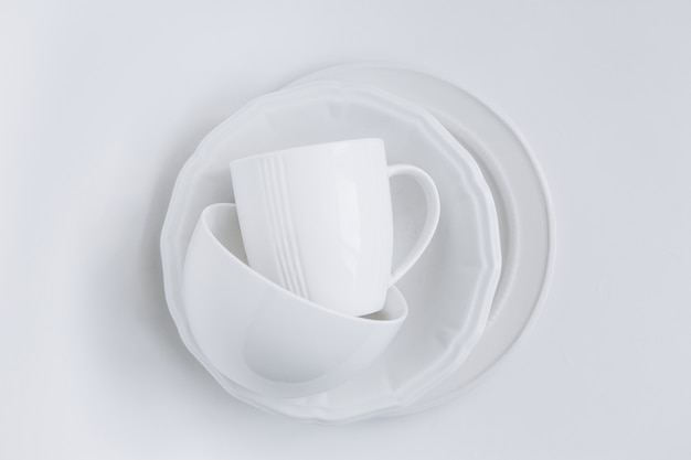 set of white utensils in a stack of three different plates and a cup